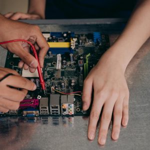Hands working with electrical tester on motherboard, showcasing technical repair skills.